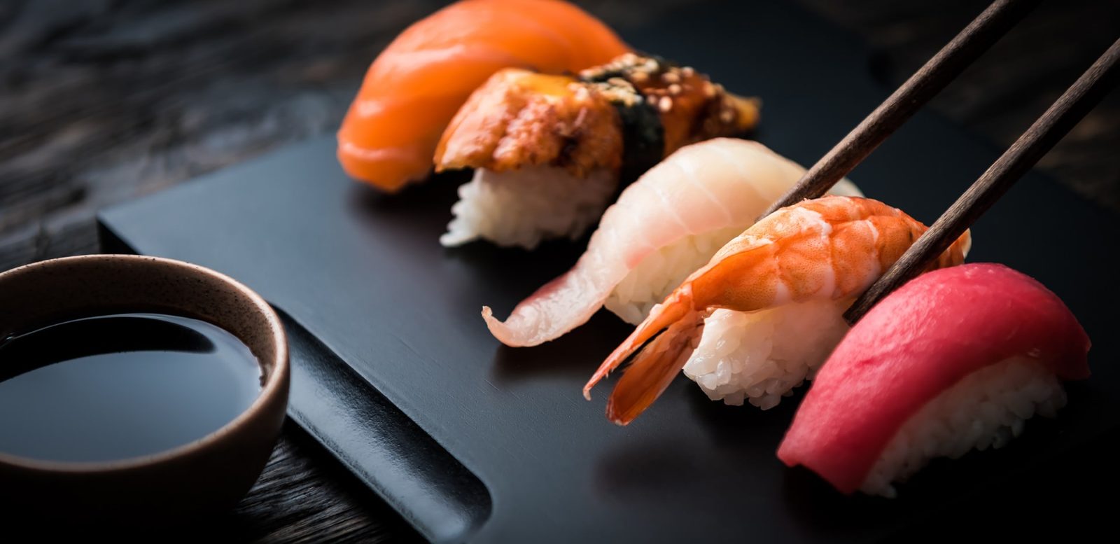 Sushi platter with chopsticks and soy sauce on dark slate